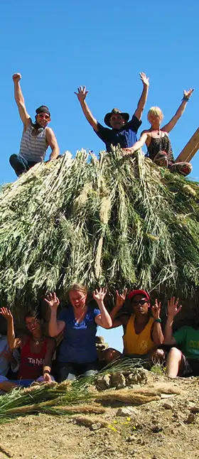 Professor on top of straw hut with class celebrating what they have created together